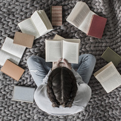 Woman sitting crossed legged reading lots of books