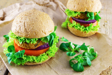 Fresh vegan sandwich with bread ciabatta onion, tomatoes, lettuce, beans cutlets on wooden background.