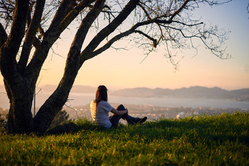 Chica joven observando la ría de Vigo a los pies de un árbol al atardecer