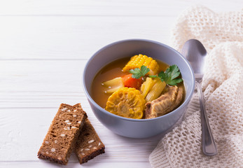 Puchero soup with corn and parsley on wooden table