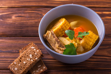 Puchero soup with corn and parsley on wooden table
