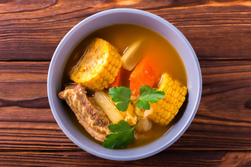 Puchero soup with corn and parsley on wooden table