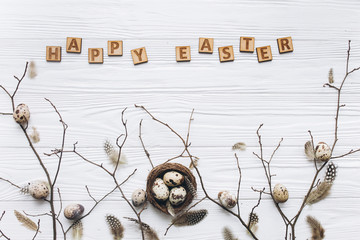 Quail eggs and feathers in the nest and wooden text for Happy Easter on white background.