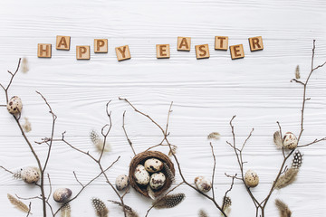 Quail eggs and feathers in the nest and wooden text for Happy Easter on white background.