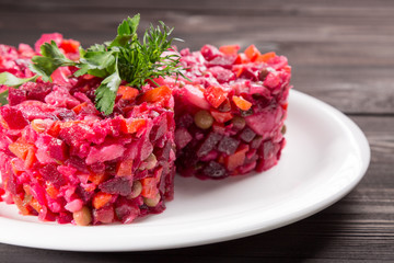 Vinegret close up - traditional Russian beet salad and vegetables with herbs on white plate and wooden table