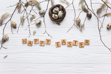 Quail eggs and feathers in the nest and wooden text for Happy Easter on white background.