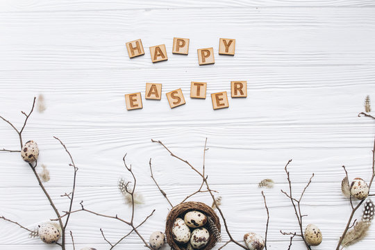 Quail eggs and feathers in the nest and wooden text for Happy Easter on white background.