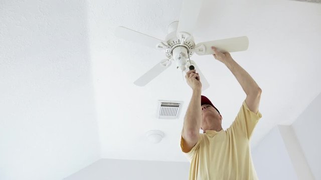 An electrician or homeowner handyman type checking the ceiling fan he has just finished installing.