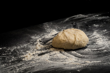 Dough on a dark black background. Baking bread, pizza, pasta. Recipe from chef cooks pizza. Italian home cooking. Top view, horizontal photo. 