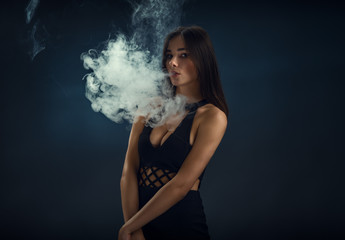 Sexy girl in a black dress smoking electronic cigarette