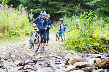 Obraz premium Young woman with her children on bikes wade the mountain creek