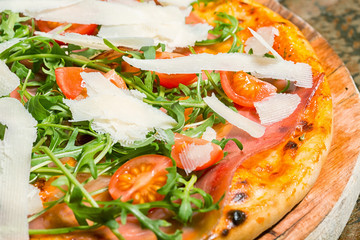Pizza with ham, tomatoes, parmesan and arugula