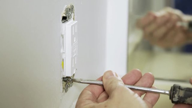 An electrician or homeowner handyman type completing the installation of a new ground fault outlet