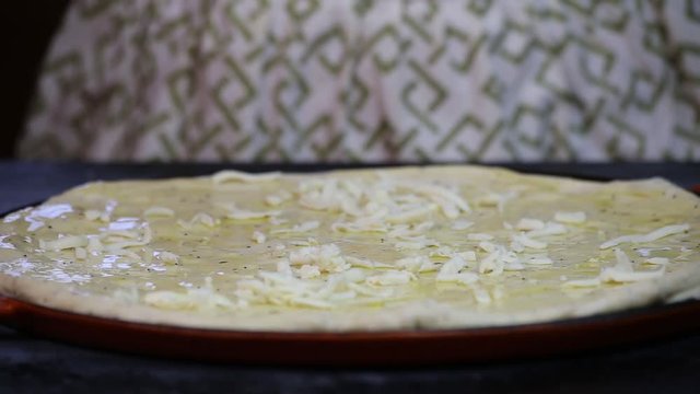 Adding shredded mozzarella cheese to a fresh pizza dough.