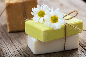 Handmade soap bars and chamomile on wooden background