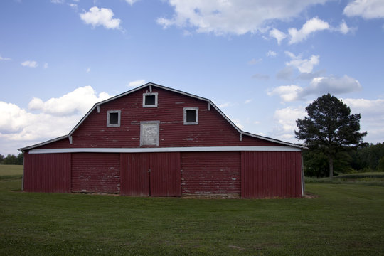 Large, beautiful red barn on bright green grass, surrounded by cloudy blue sky