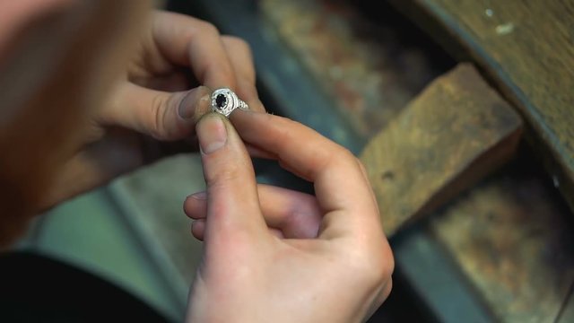Jeweler holds a finished silver ring in his hands and continues polishing