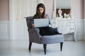 Young woman at home in the armchair relaxing in her lliving room with laptop