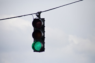 Green traffic light surrounded by overcast sky.