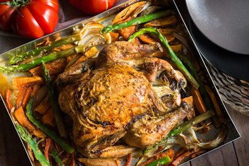 Table set for dinner, home cooked roasted chicken with vegetables sweet potatoes, carrots, asparagus, onions, tomatoes, top view