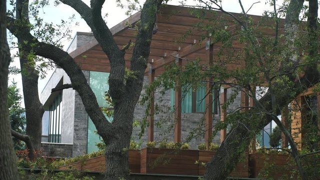 Living resort building with stone siding and wooden patio in forest green leaves and pines, summer time cloudy day, tracking shot