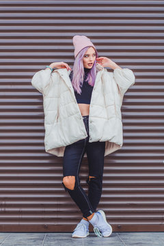A beautiful girl with purple hair walks the streets of the city. Wearing a jacket, torn jeans and a hat.