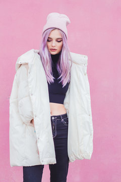 A beautiful girl with purple hair walks the streets of the city. Wearing a jacket, torn jeans and a hat.