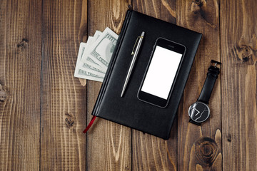 Business Concept - Top view of smartphone, watch, pen, notebook and money on wooden background.