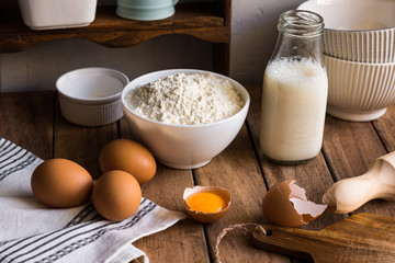 Fototapeta na wymiar Traditional baking ingredients flour milk organic eggs on wood kitchen table in rustic rural interior, utensils, authentic style