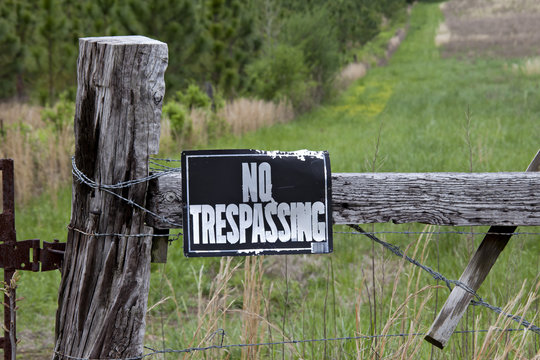 No trespassing sign on weathered fence post in front of a green field.