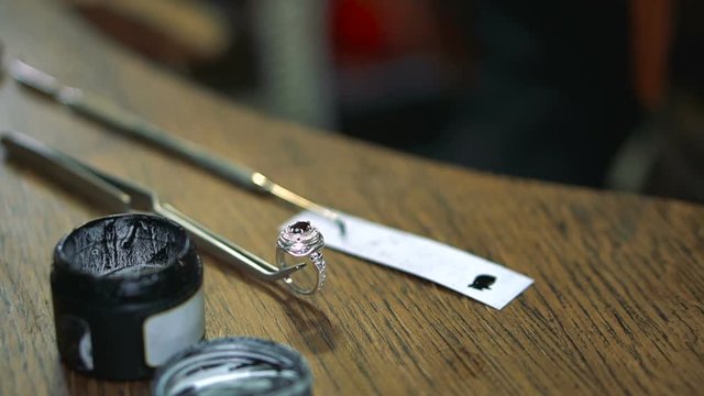 Silver ring fixed in special tongs lies on a wooden table next to the can of enamel for painting
