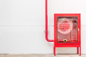 Red fire hose cabinet and extinguisher on white wall in the new building factory with copy space...
