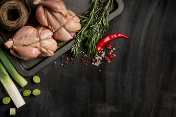 Chicken on a baking sheet with greens, herbs and spice before baking in the oven. Food on a dark background for a book of recipes or design. Horizontal. Text area. Top view., flat, overhead. © Anton