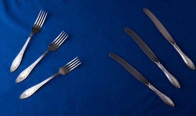three silver knifes and forks on blue table cloth