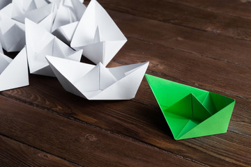 Business leadership concept with white and color paper boats on wooden table