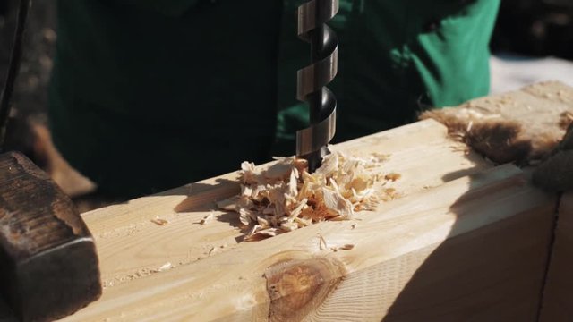 Close up drilling big hole in wooden block creating sawdust outside in winter, snow on background