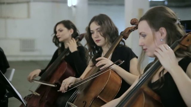 Three girl play on violoncello in orchestra