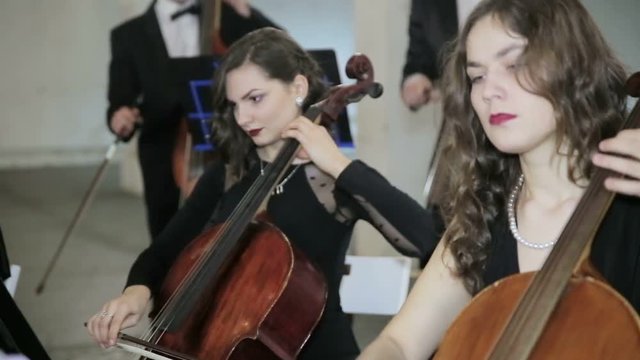 Girls play on violoncello in orchestra