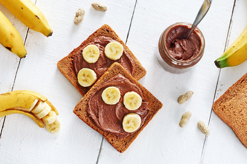 Portion of chocolate peanut butter sandwiches with rye bread and bananas over white background. Healthy snack with saturated fats. Top view.