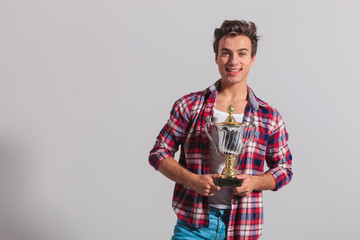 happy young casual man holding a trophy cup