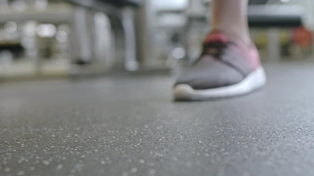 Ground level shot with selective focus of hands of female athlete picking up 3 kg dumbbell from gym floor
