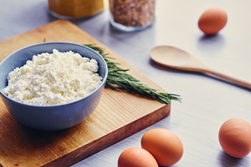 Curd in a cup, eggs and wooden spoon lying on a table.