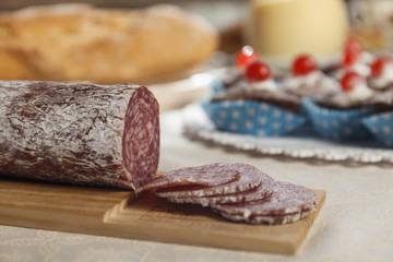 Close up of sliced sausage salame. Muffins, cheese and fresh bread in the background. Breakfast time