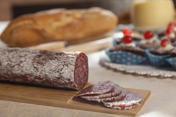 Close up of sliced sausage salame. Muffins, cheese and fresh bread in the background. Breakfast time