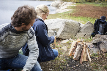 Man Looking At Woman Chopping Wood On Campsite