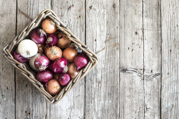 Raw onions in basket on wooden table