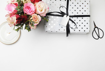 Flay lay. White table bouquet roses scissors bonsai festive and white tag holiday. Female desktop, gift and pattern polka dots.
