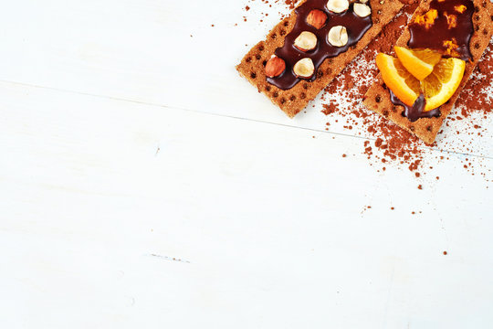 Healthy snack: homemade sandwiches with chocolate, hazelnut and oranges on a rye crispbread over white table. Copy space.