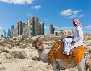 Bedouin on a camel in the desert and a modern city on the horizon
