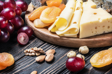 Cheese plate with fruits and nuts on a wooden table